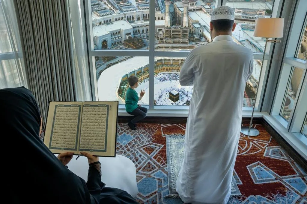 Familie betet im Hotelzimmer mit Blick auf die Kaaba